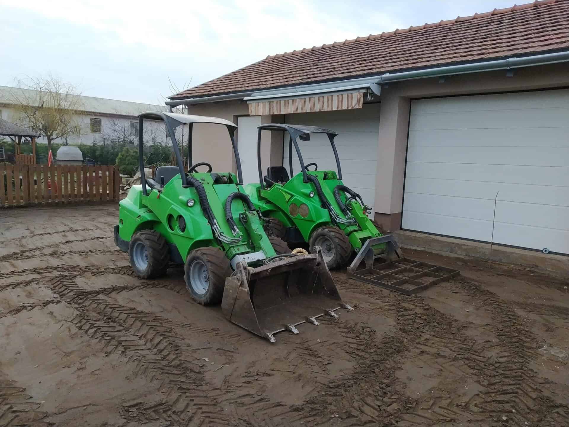 Két zöld mini kotrógép a kertben, felkészülve a tereprendezésre.