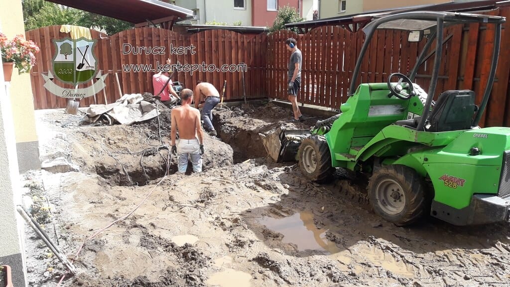 Támfal építés folyamatban, munkások és gép dolgozik a területen.