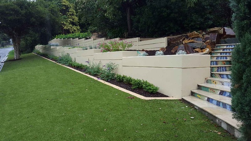 Modern támfal építése kertben, lépcsővel és növényekkel.