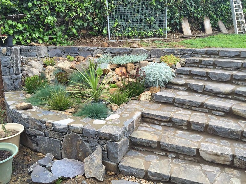 Sziklakert kialakítás lépcsőkkel és növényekkel, tartós kőburkolattal.