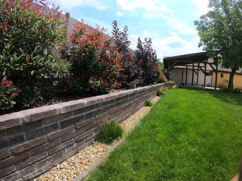 Álló kép egy magaságyásról, amelyet kőből építettek, a kertben, a növények és a zöld fű mellett.