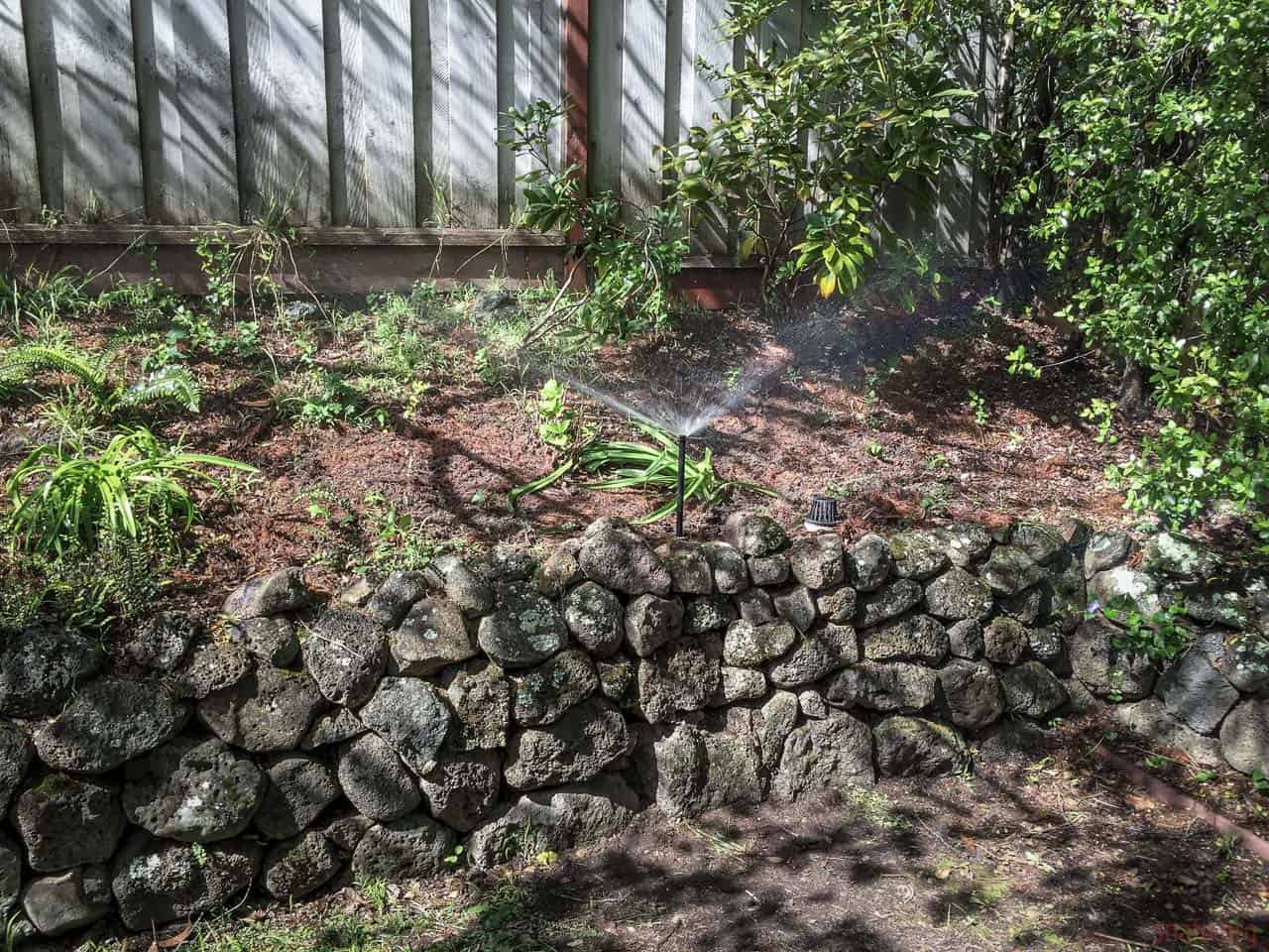 Támfal építése kőből a kertben, növények és fák között.